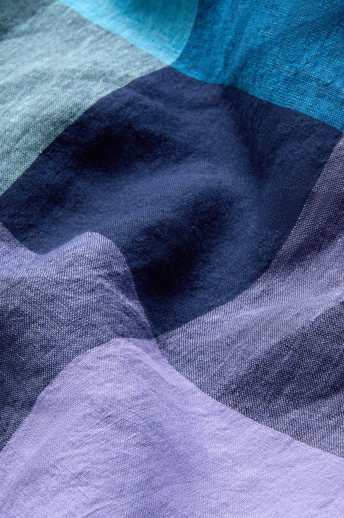 A close-up of crumpled fabric from the Cross Dye Check Linen Maxi Dress, featuring overlapping blue, navy, and lavender patches.