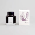 Black glass ink bottle with purple watercolor label and white presentation box.