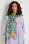 Woman with curly hair wearing a light purple dress and the Archival Stripe Silk Scarf, featuring a colorful stripe design, standing against a plain white background.