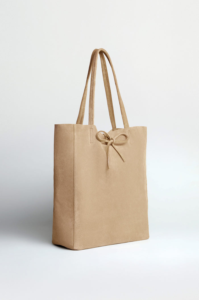 The Soft Suede Sand Tote Bag features double handles, a front bow detail, and a spacious interior, shown against a plain light background.