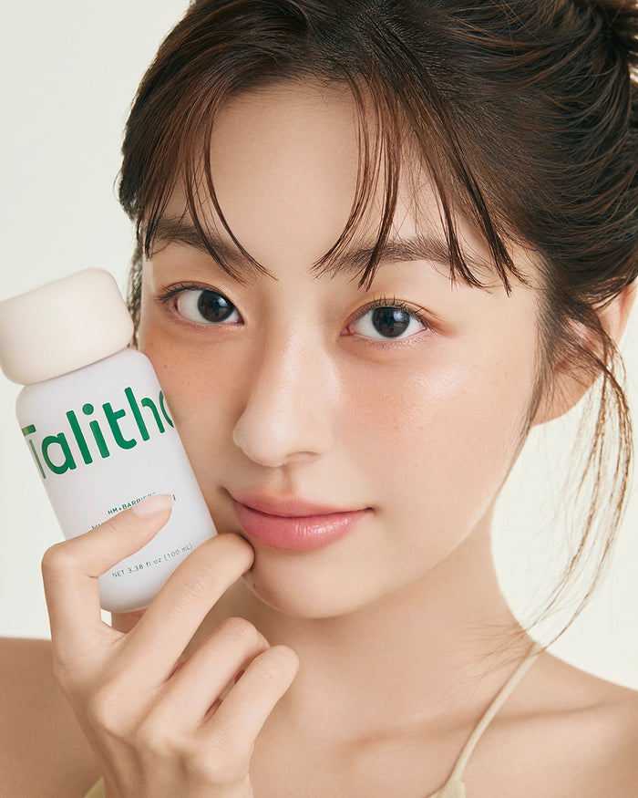 Talitha Koum essence soo bottle held near face, white cap and green label