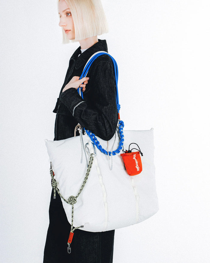 Blue braided O-rope strap on a white tote bag with orange pouch and silver chain