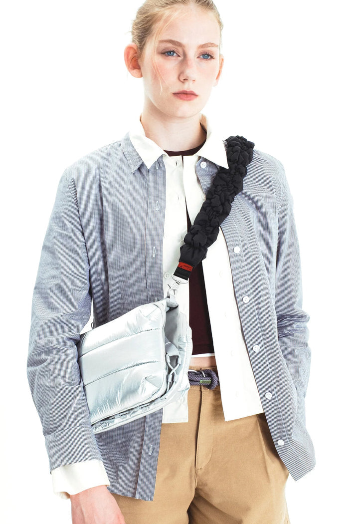 Braided dark crossbody strap with metal clips worn over a light shirt
